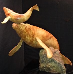 wood and stone sculpture of momma whale helping baby get first breath